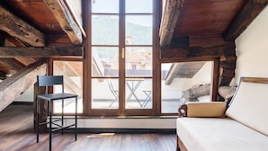Um quarto com pé direito alto, vigas de madeira aparentes, uma janela grande, um sofá e uma mesa pequena.