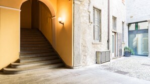 Uma escadaria leva a um espaço interior, um edifício com fachada de pedra e um pequeno pátio com uma planta em vaso.
