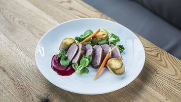 A white plate with sliced meat, potatoes, and greens on a wooden table.