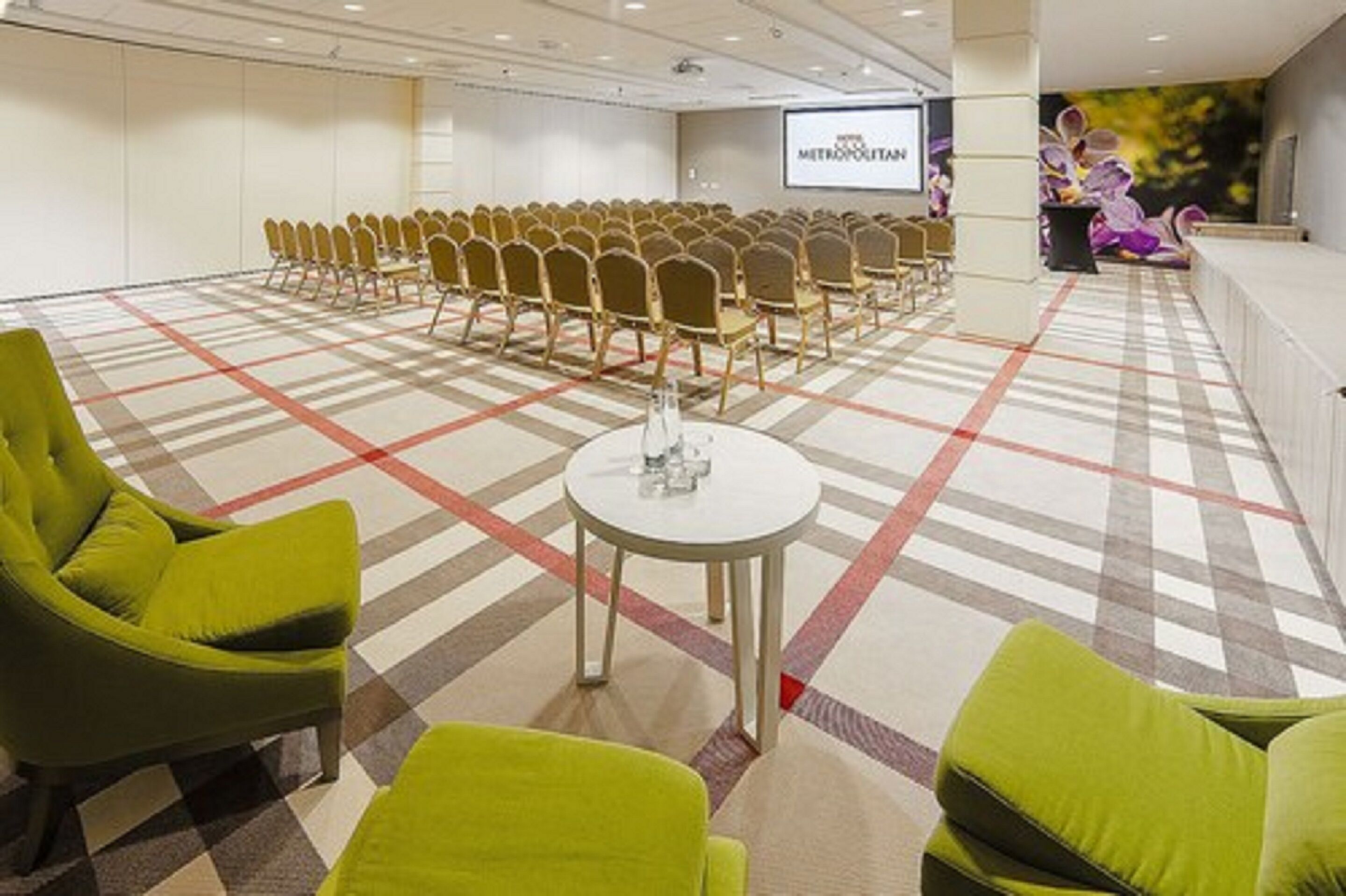 Une salle de conférence avec des rangées de chaises, un écran de projection et une scène agrémentée d’un décor floral.