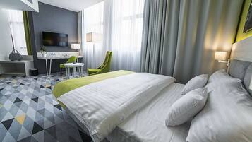 A hotel room with a large bed, a desk with a chair, a television, and a window with curtains.