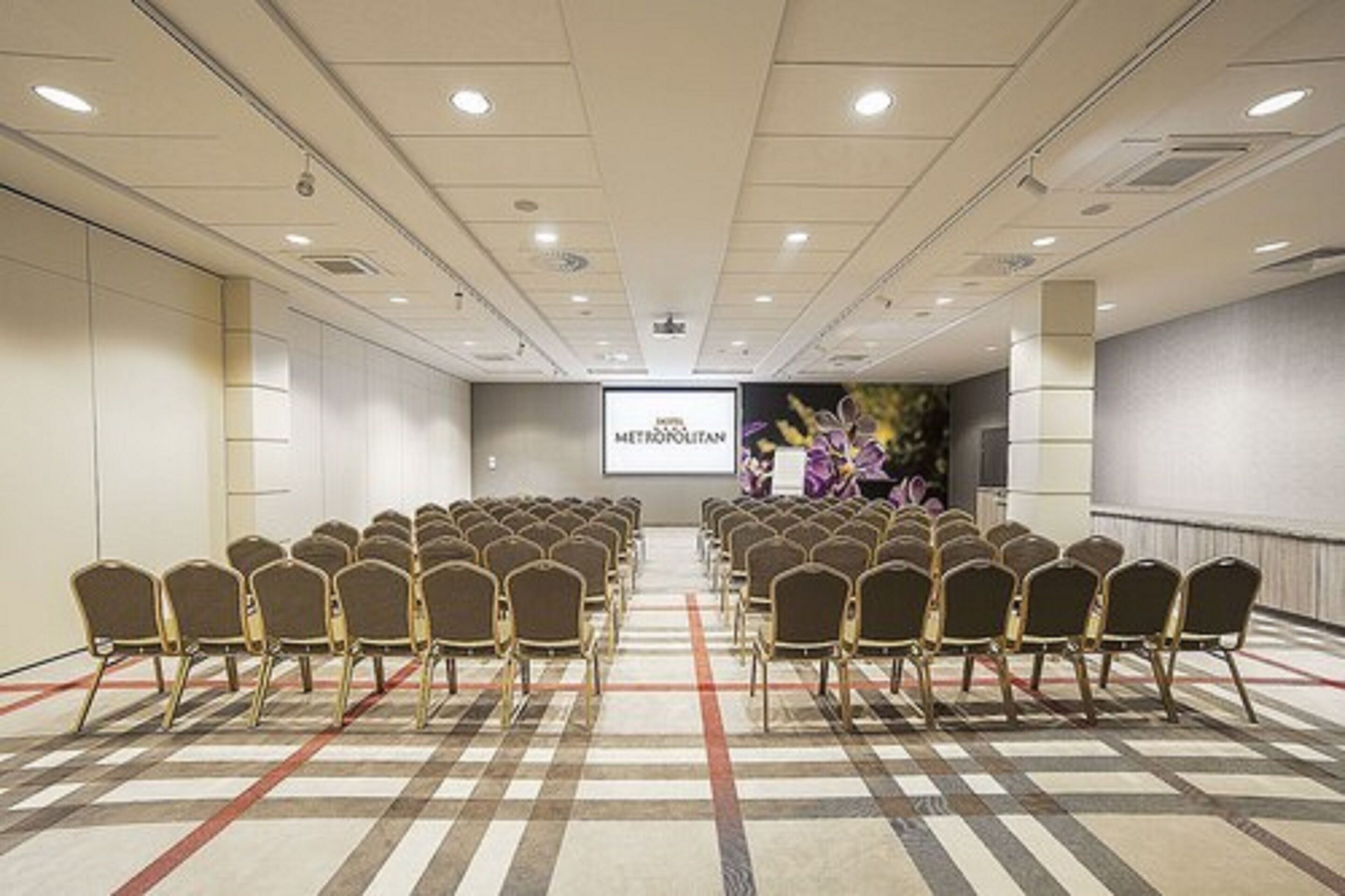A conference room with rows of chairs facing a projection screen displaying 'HOTEL METROPOLITAN'.
