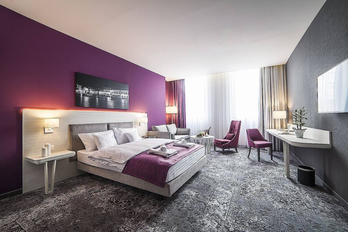 A hotel room with a large bed, a desk, a chair, and a small table.