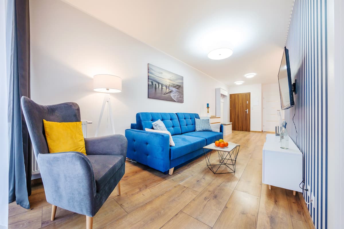 A modern living room with a blue sofa, a grey armchair, and a small coffee table with fruit.
