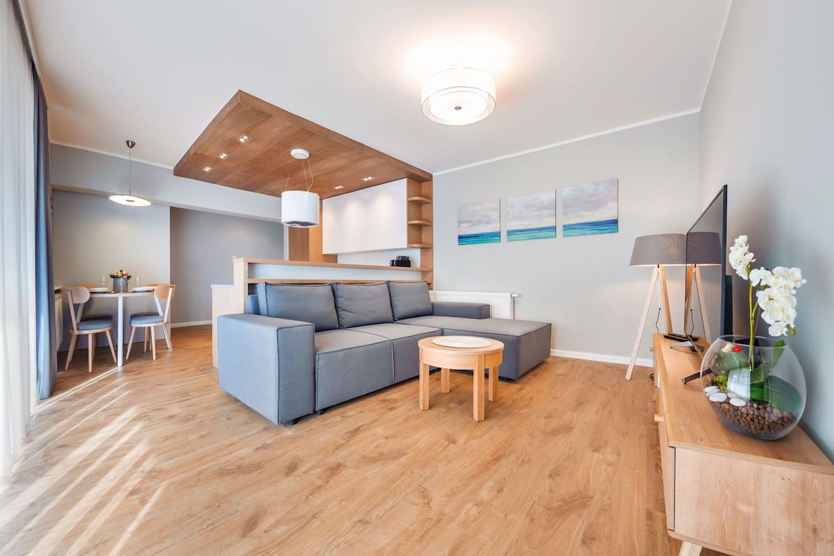 A modern living room with a grey sectional sofa, a wooden coffee table, and a dining area with a table and chairs.