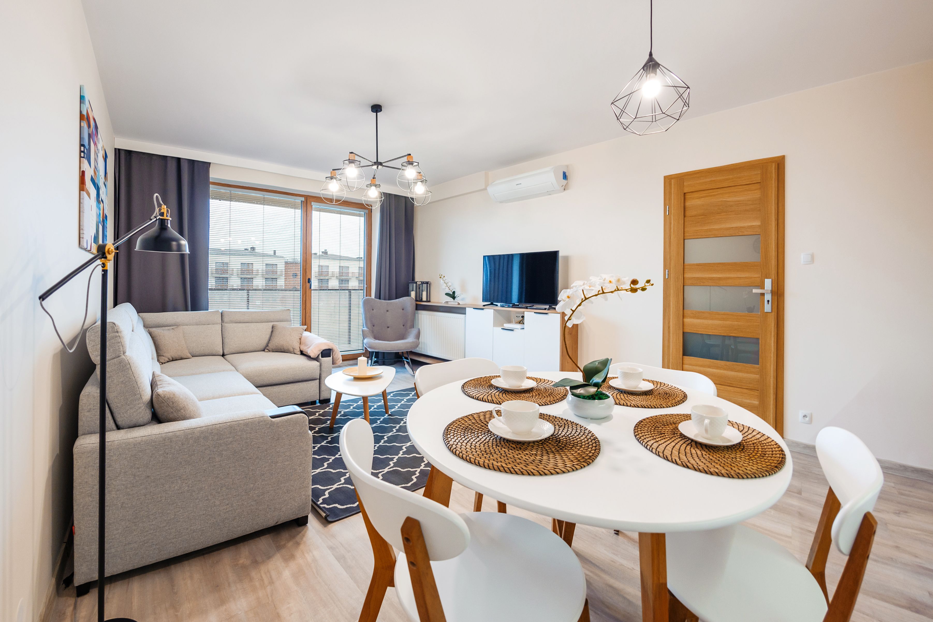 Una sala de estar moderna con un sofá, una mesa de comedor con individuales, un televisor y una puerta de madera.