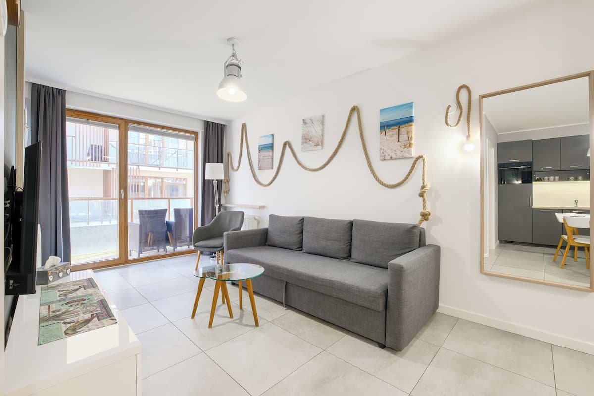 A modern living room with a grey sofa, a glass coffee table, a lamp, and a large mirror on the wall.