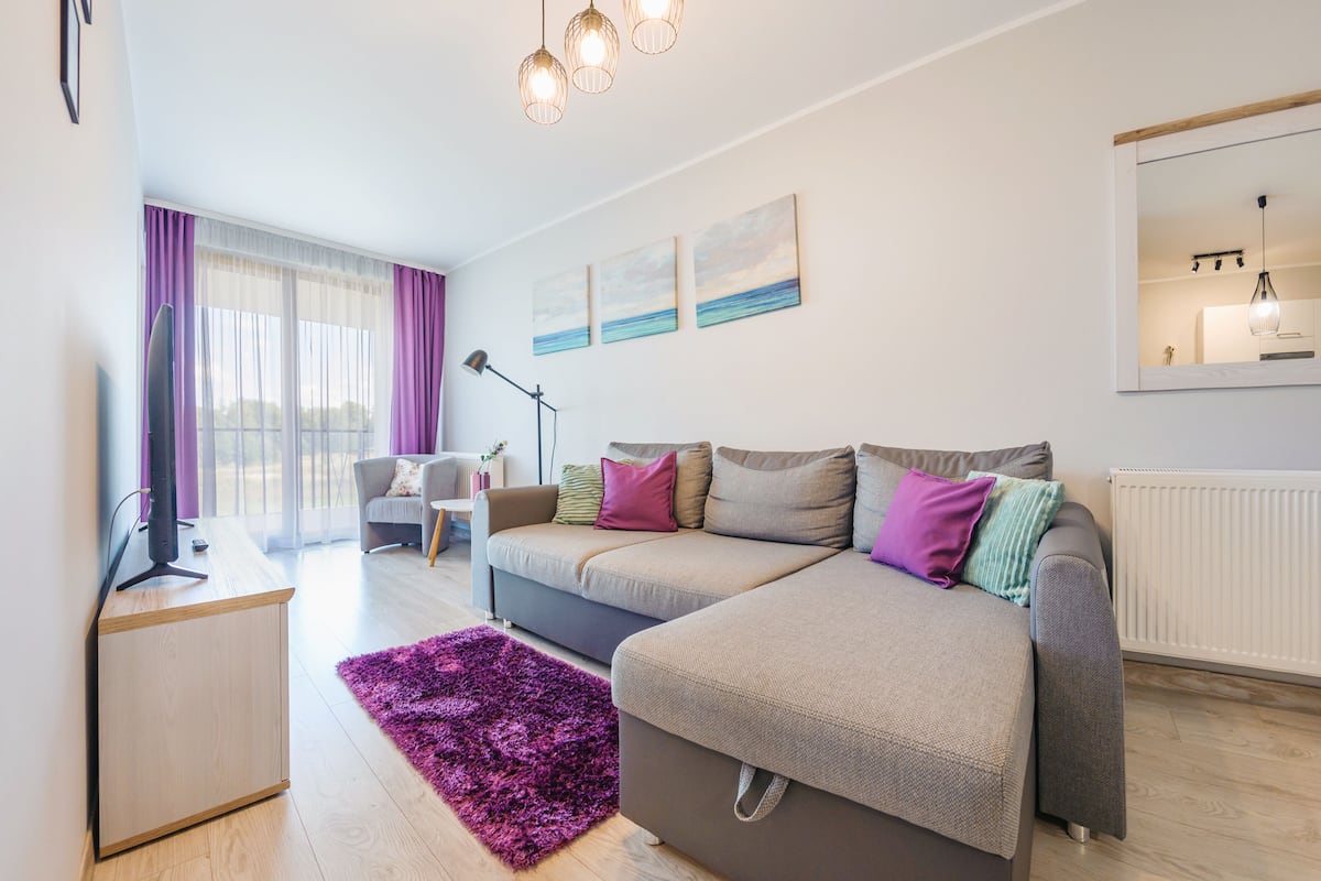 A modern living room with a sofa, a coffee table, a TV, and a large window with curtains.