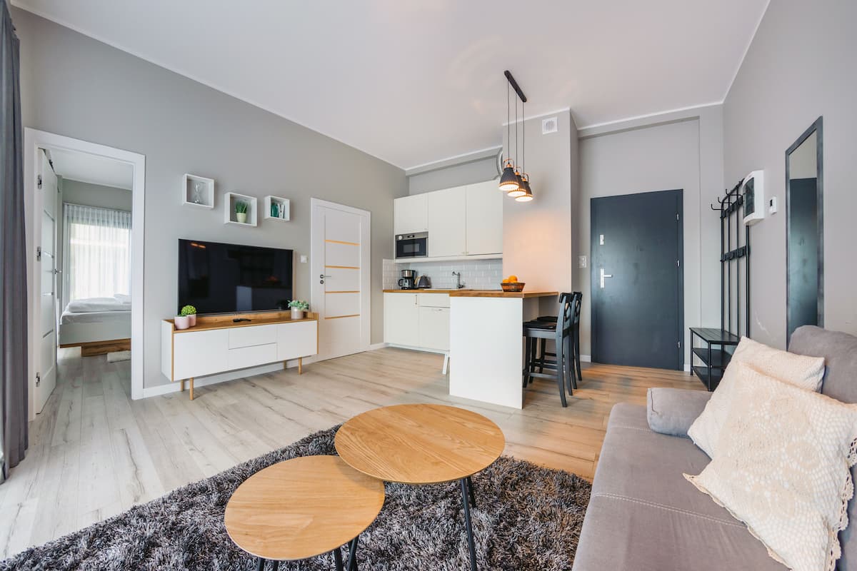 Eine moderne Wohnung mit Wohnzimmer, Küche und Essbereich. Sie verfügt über einen Fernseher, eine Couch und einen kleinen Esstisch.