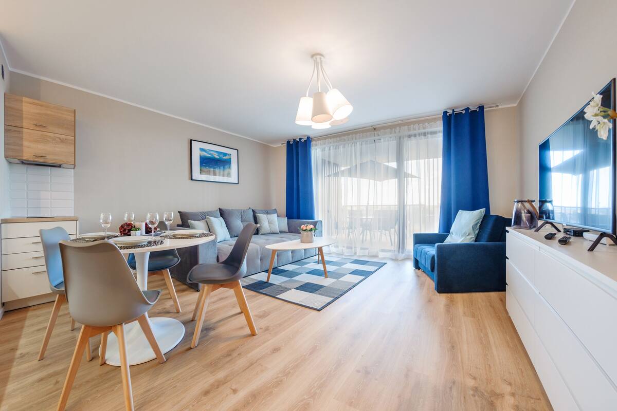 A modern living room with a dining area, a sofa, a TV, and a kitchen area with wooden cabinets.