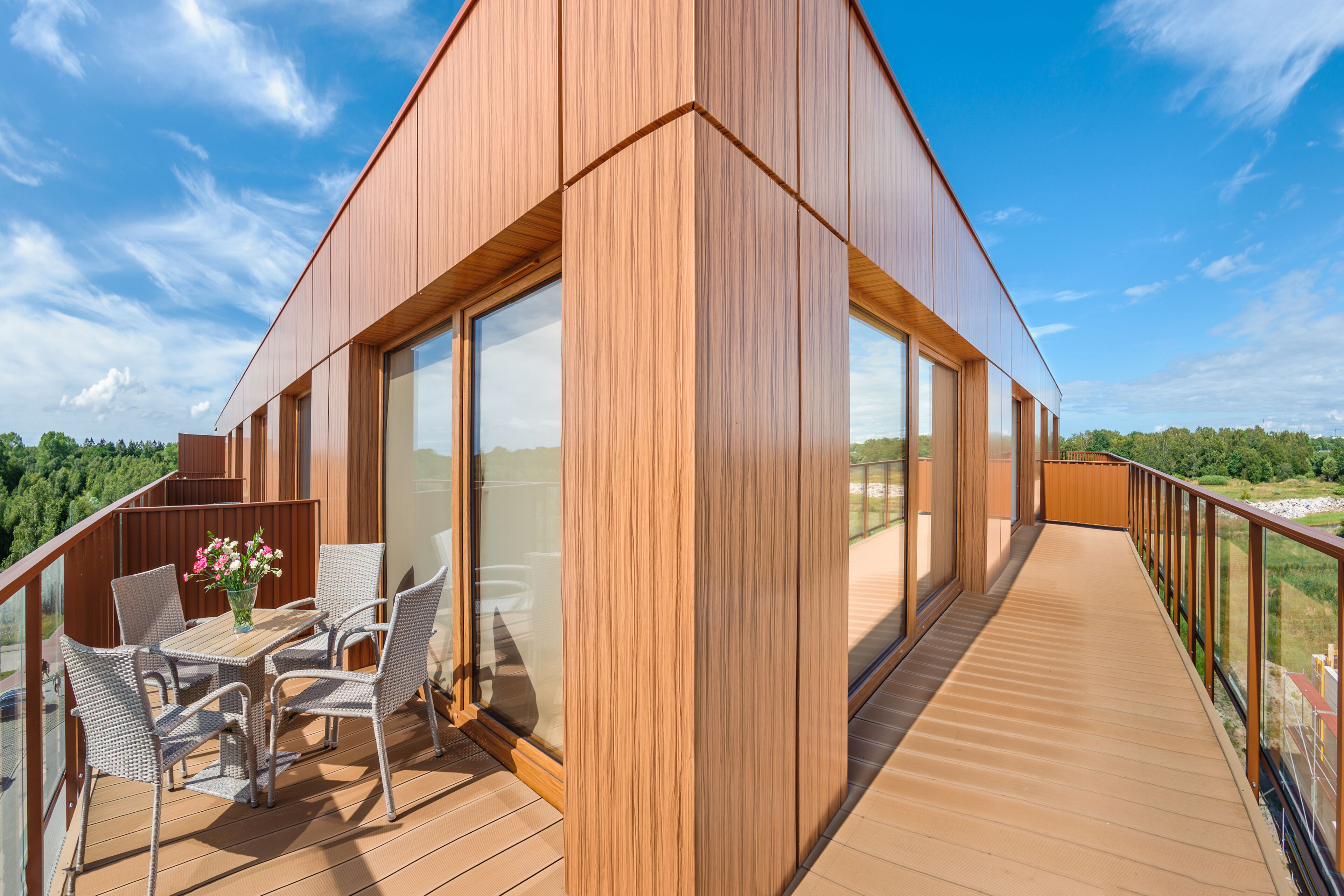 Un edificio moderno con fachada de madera, amplias ventanas y un balcón con mobiliario exterior.