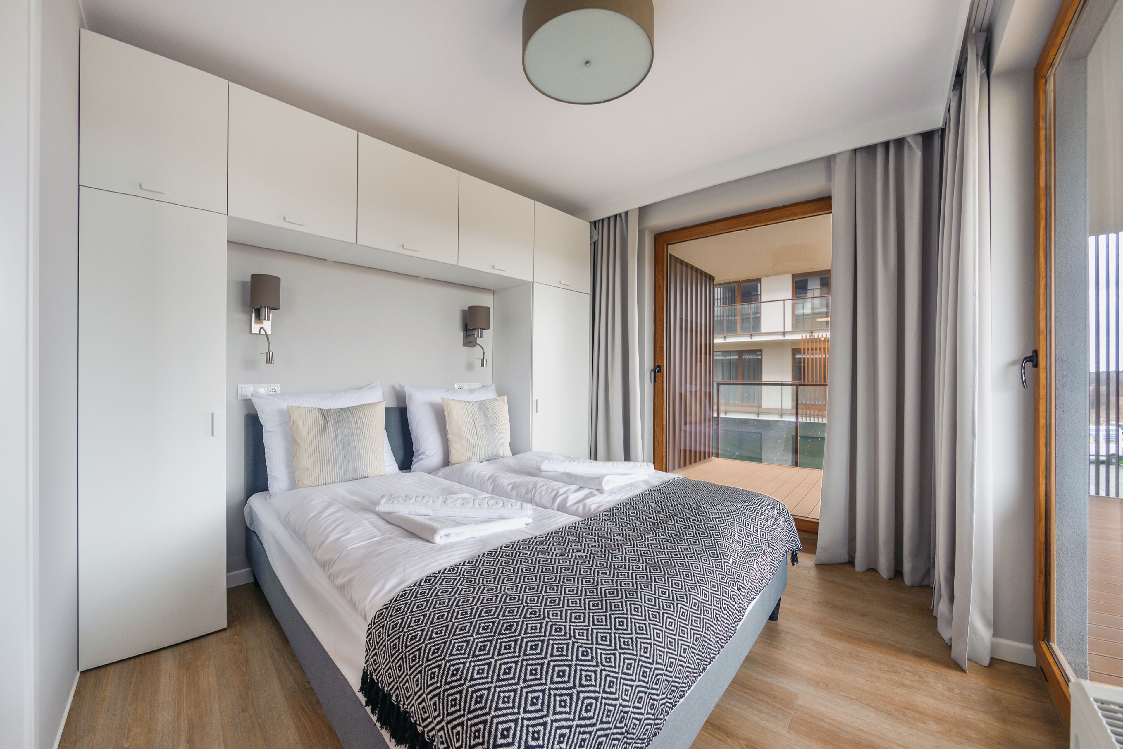 A modern hotel room with a large bed, built-in wardrobe, and a balcony with curtains.