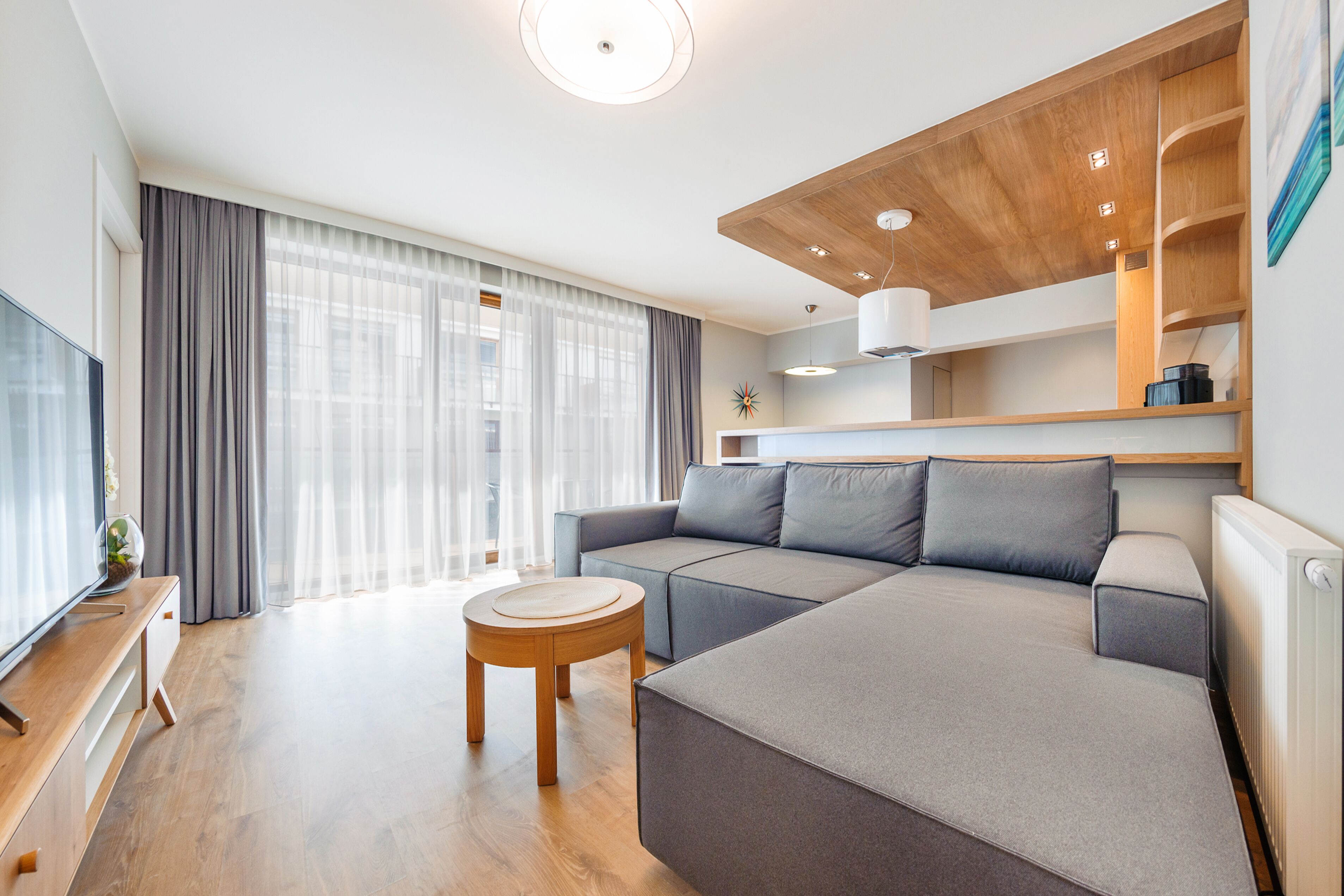 Un salon moderne avec un canapé d’angle, une table basse en bois et un téléviseur posé sur un meuble en bois.