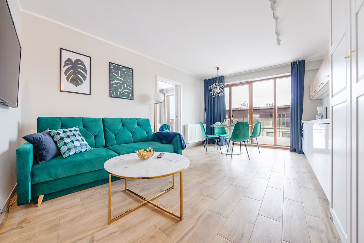A modern living room with a green sofa, a round coffee table, and a dining area with a table and chairs.