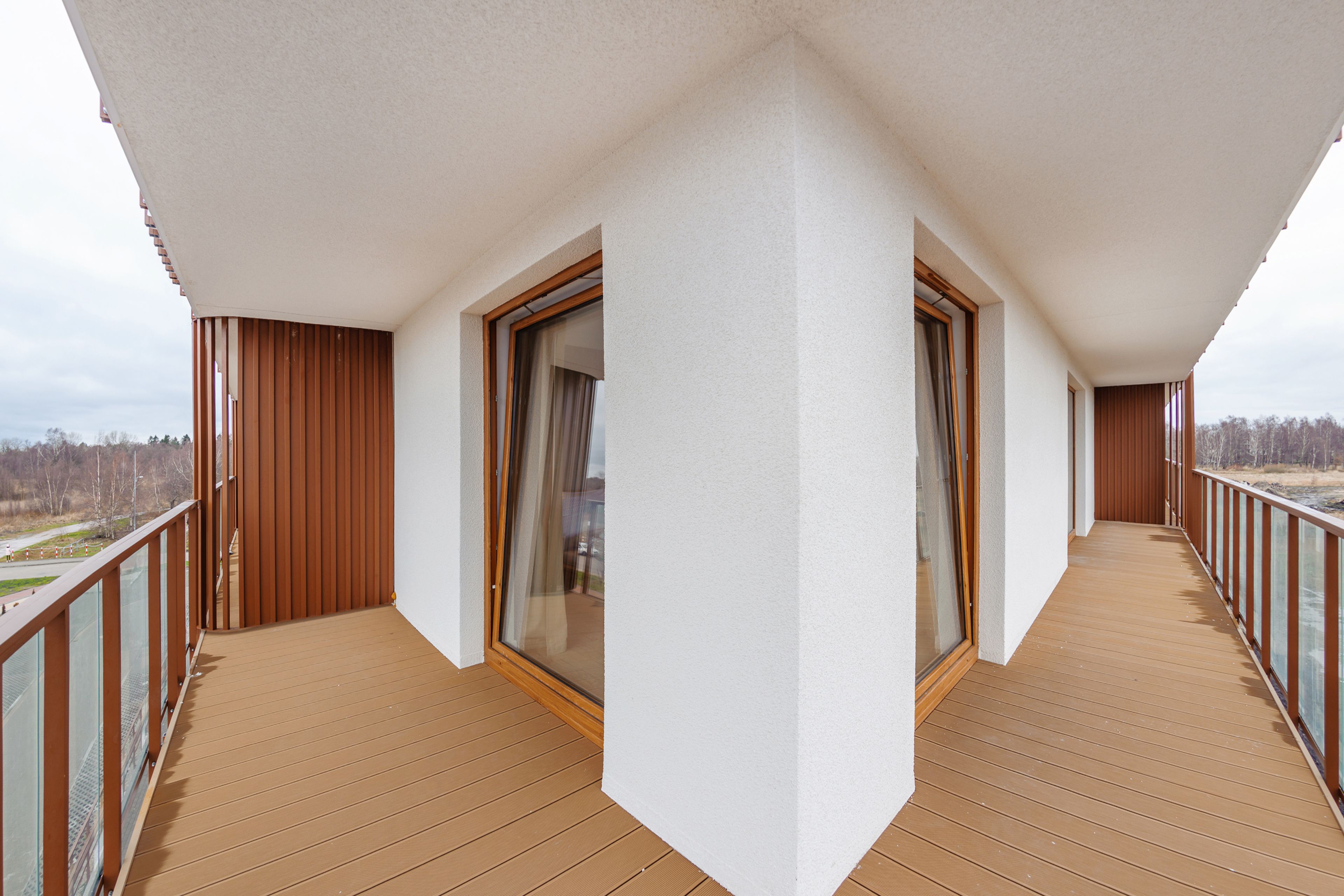 Een balkon met een houten vloer, glazen deuren en uitzicht op de omgeving.