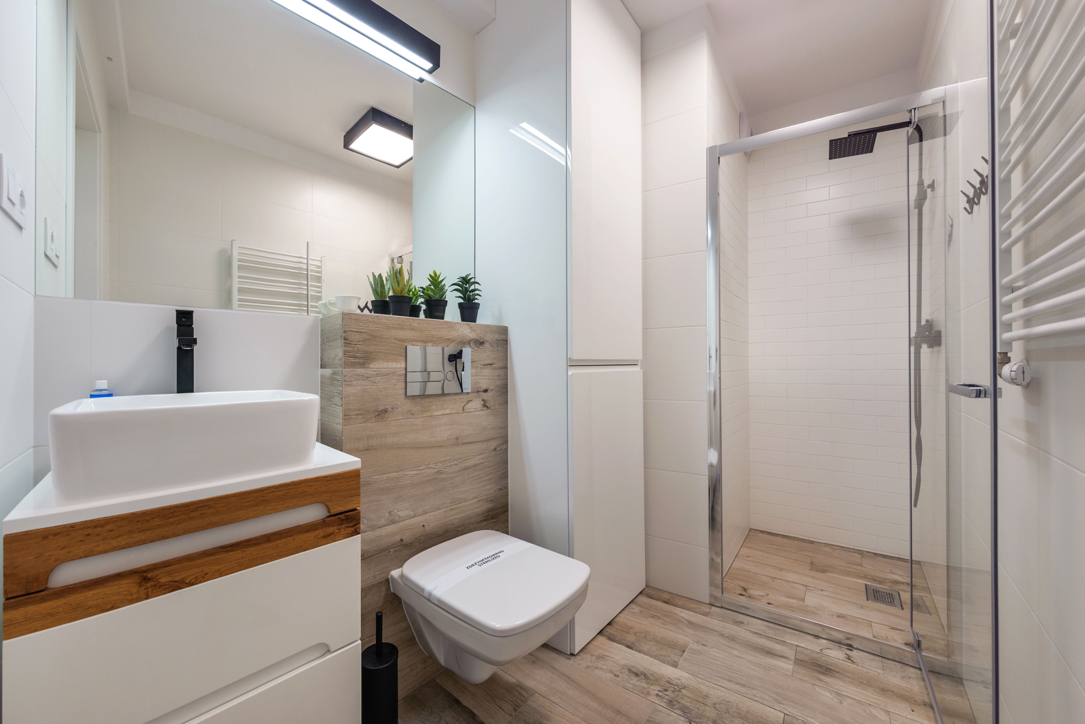 Un baño moderno con lavamanos blanco, tocador de madera, inodoro y zona de ducha con mampara de cristal.
