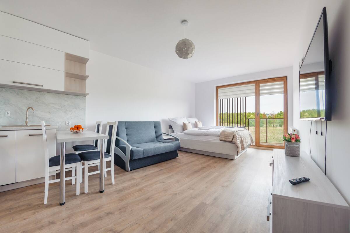Ein moderner, gut beleuchteter Raum mit Essbereich, einer Couch und einem an der Wand befestigten Fernseher.