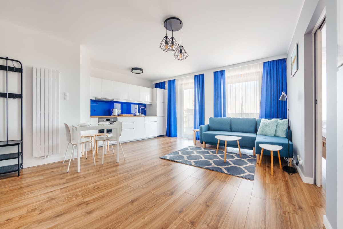 Ein modernes Wohnzimmer mit einem blauen Sofa, einem Esstisch mit Stühlen und einer Küche im Hintergrund.