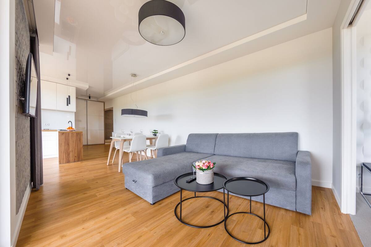 Ein modernes Wohnzimmer mit einem grauen Ecksofa, zwei runden Tischen in Schwarz und einem Holzboden.