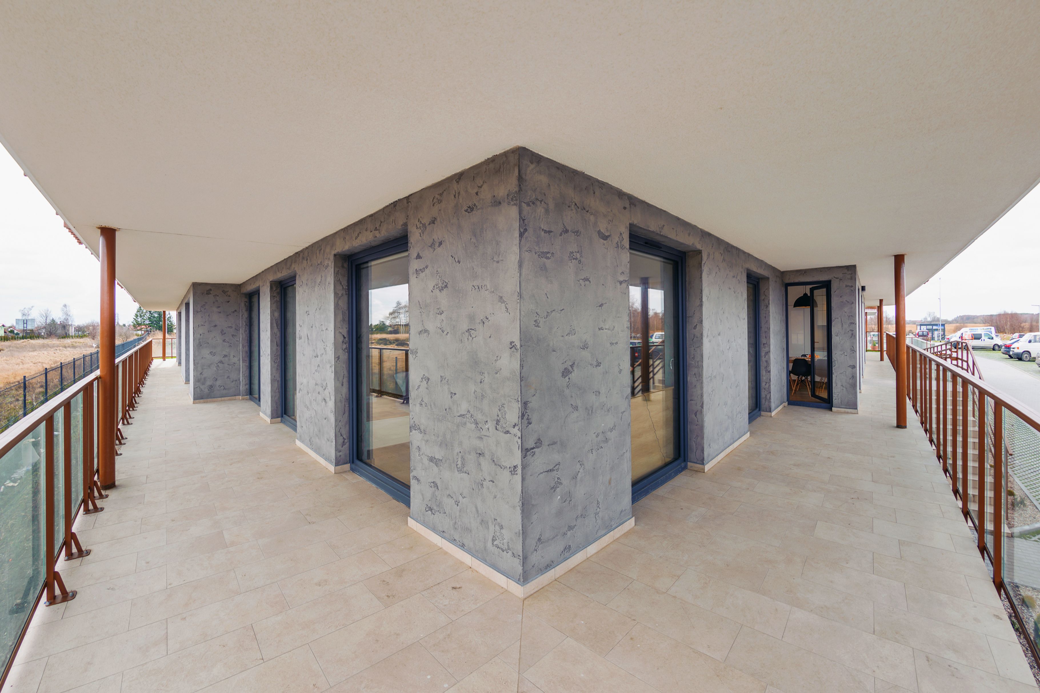 A spacious balcony with a modern design, featuring a large central column, glass doors, and a metal railing.