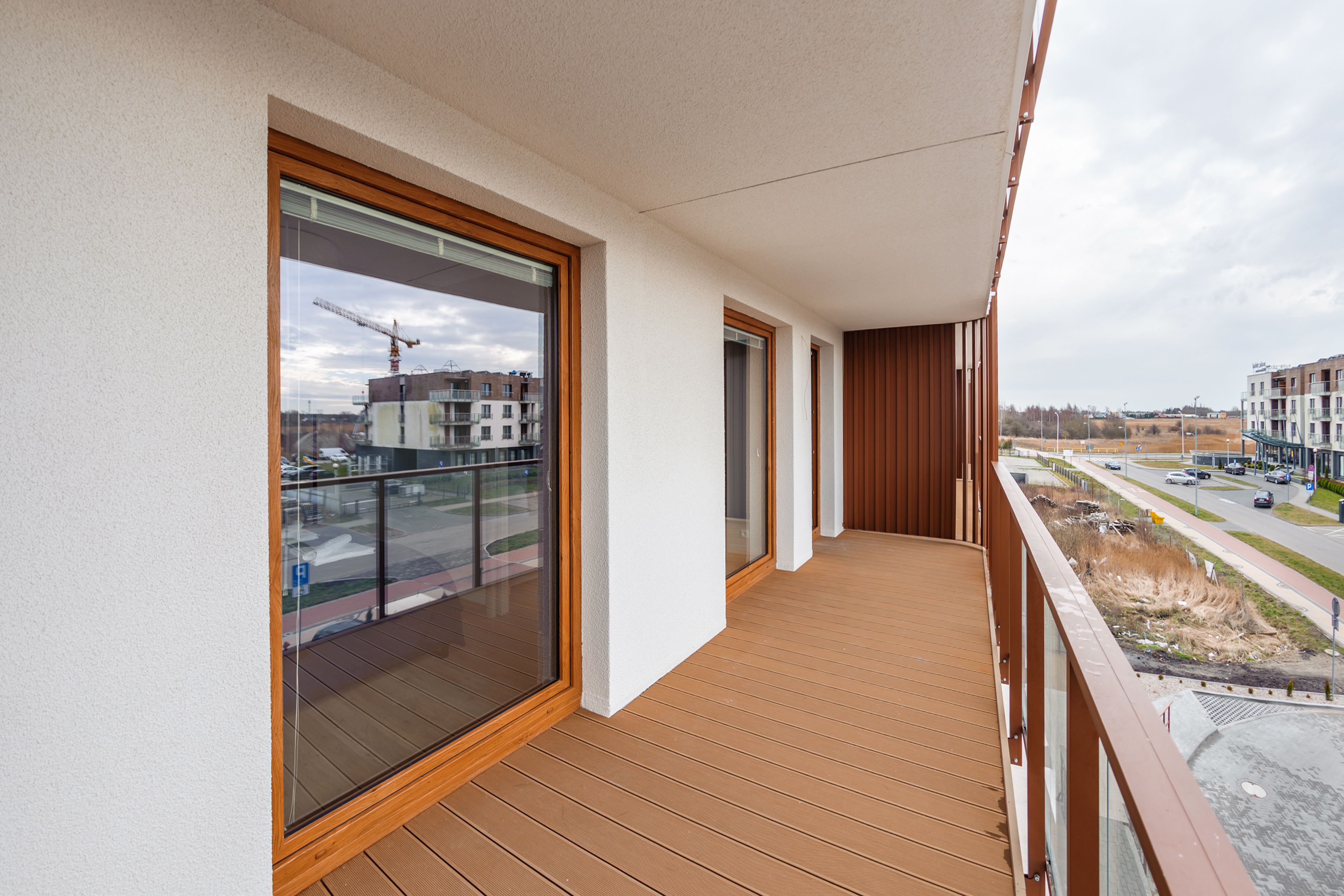 Un balcón con suelo de madera, ventanas grandes y vista a una obra en construcción.