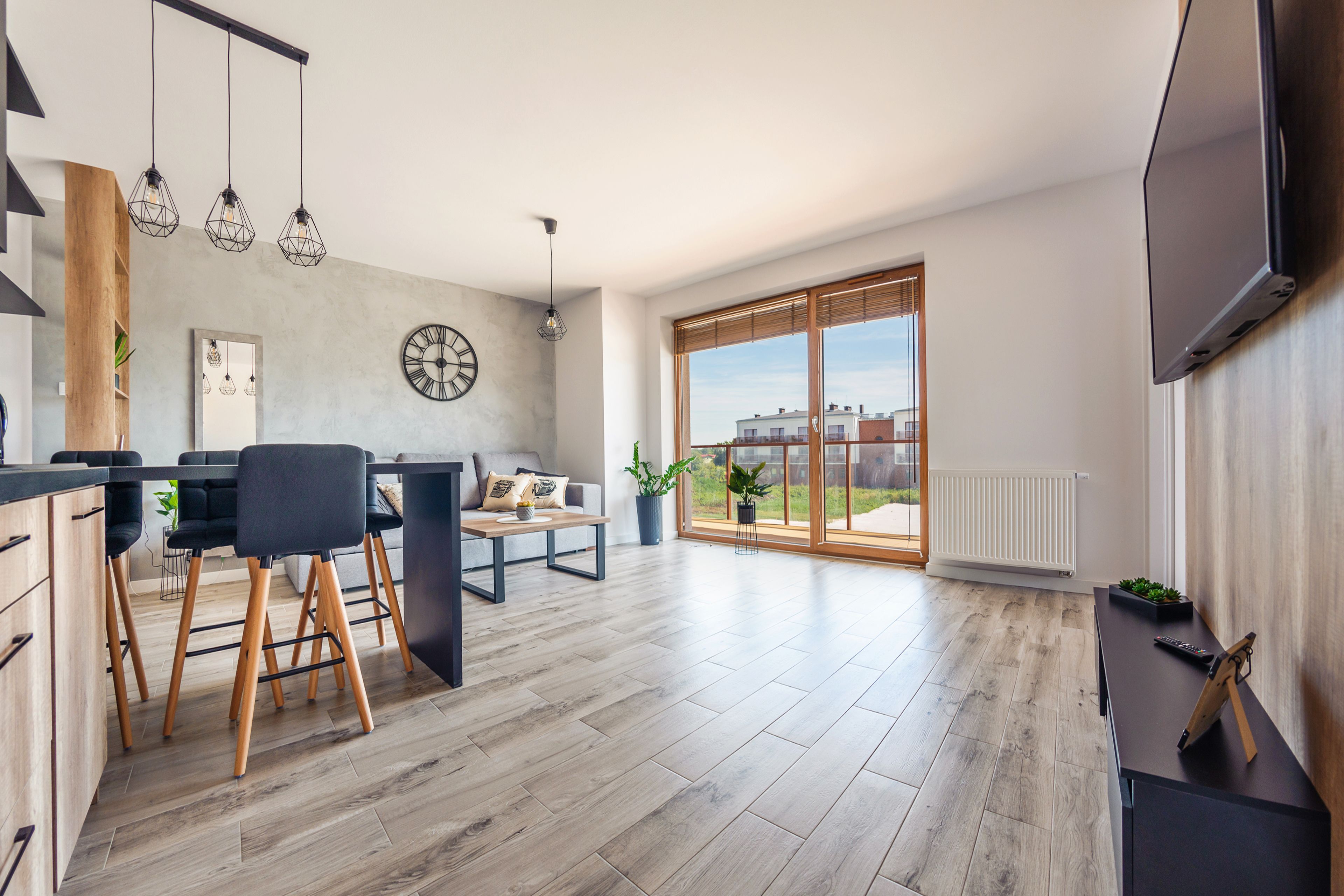 Une cuisine moderne avec un plancher en bois, un coin repas avec un banc et des chaises, une grande fenêtre offrant une belle vue, et un téléviseur à écran plat fixé au mur.
