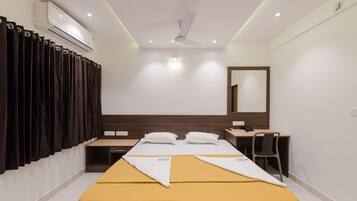 A hotel room with a bed, a desk, a chair, an air conditioning unit, a ceiling fan, and a mirror.
