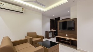 A modern living room with a flat-screen TV, leather sofas, a coffee table, and a ceiling fan. - Hotel Karuna Residency (Mangaluru)