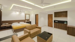A modern hotel room with a bed, sofa, and a small table. There is a kitchenette with cabinets and a countertop. - Hotel Karuna Residency (Mangaluru)