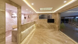 A hotel reception area with marble flooring, a reception desk, and a large window with blinds. - Hotel Karuna Residency (Mangaluru)