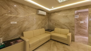 A modern waiting area with marble walls, two beige sofas, and a decorative ceiling light fixture. - Hotel Karuna Residency (Mangaluru)