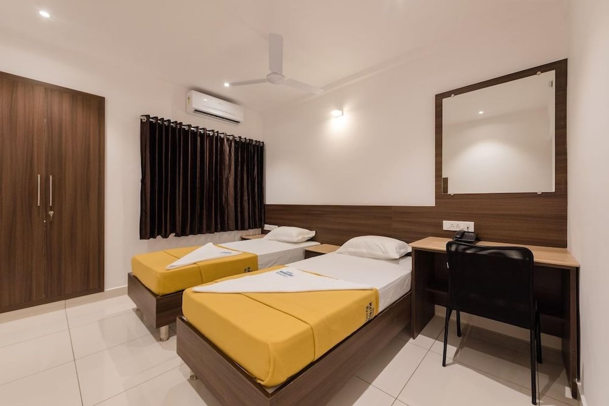 Habitación de hotel con dos camas, un escritorio, una silla, un armario y un espejo.