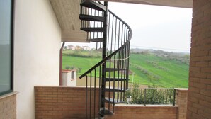 Een spiraaltrap die uitkomt op een balkon met uitzicht over een groen landschap.
