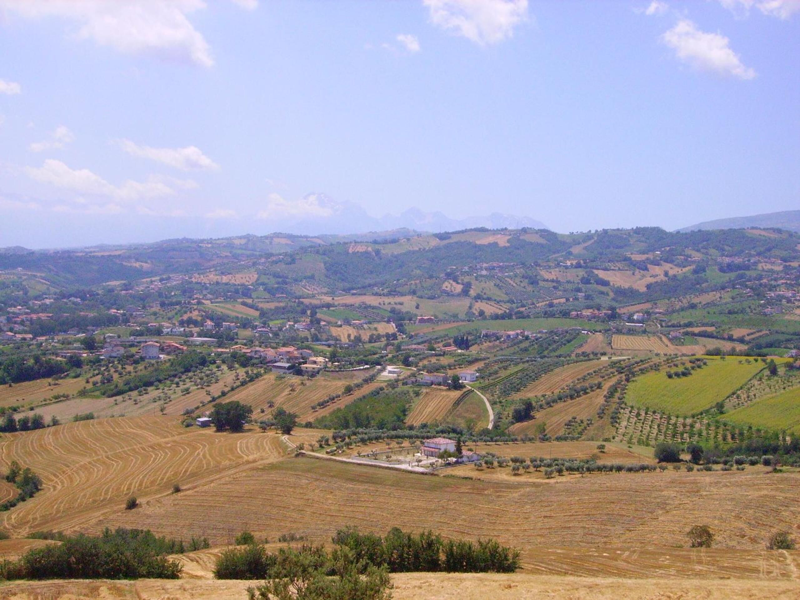 A rural landscape with rolling hills, scattered houses, and agricultural fields.
