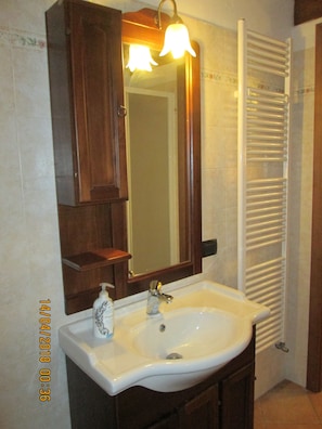 Un baño con un lavamanos blanco, un espejo encima y un perchero a la derecha.
