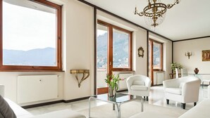 Ein geräumiges Wohnzimmer mit großen Fenstern, weißen Möbeln und einer Chandelüster.