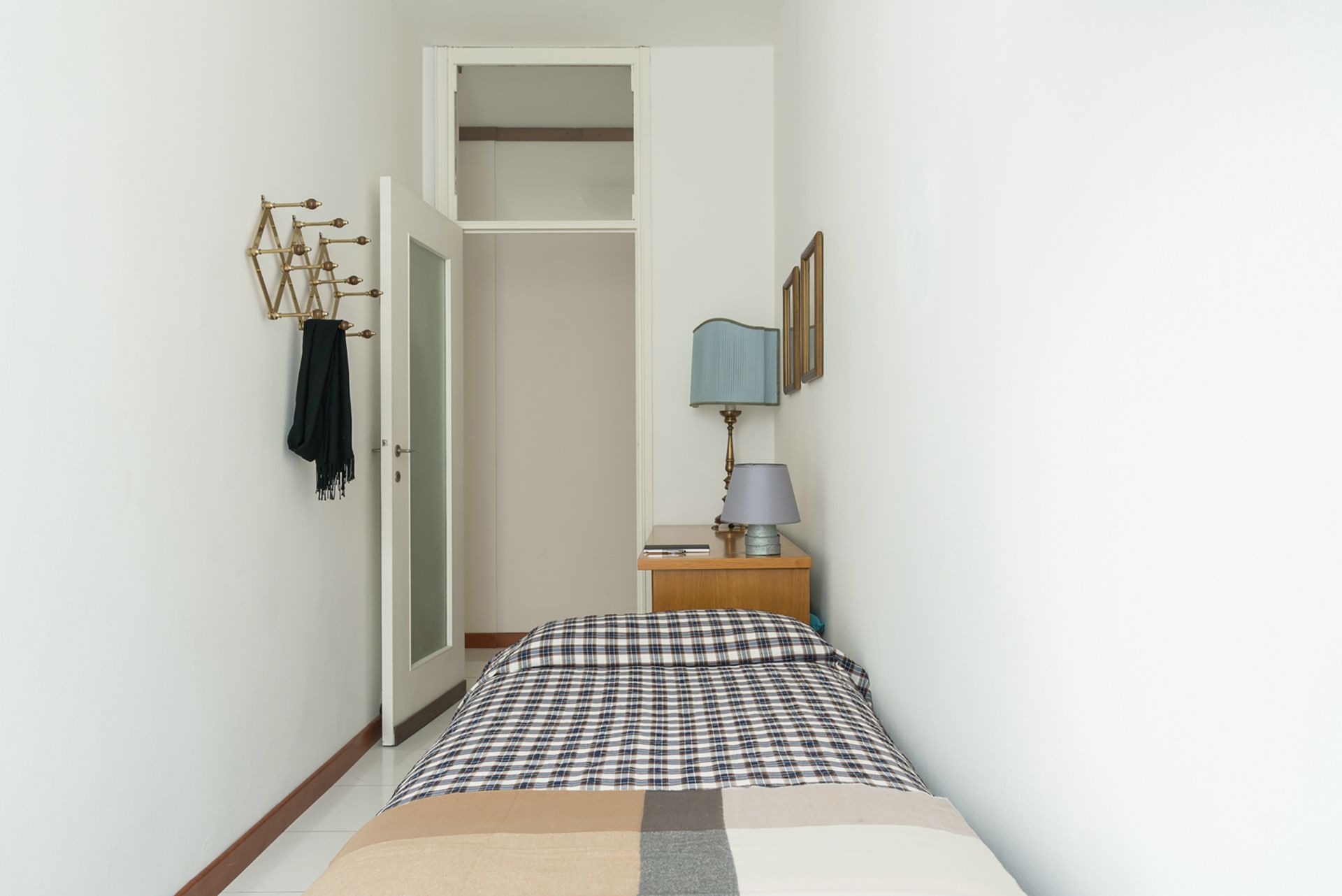 A bedroom with a bed, a nightstand, a lamp, a wardrobe, and a coat rack.