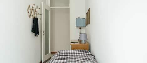 A bedroom with a bed, a nightstand, a lamp, a wardrobe, and a coat rack.