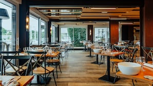 A restaurant with wooden tables and chairs, large windows, and a view of the city.