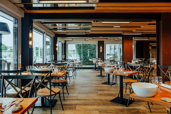 Um restaurante com mesas e cadeiras de madeira, janelas amplas e vista para a cidade.