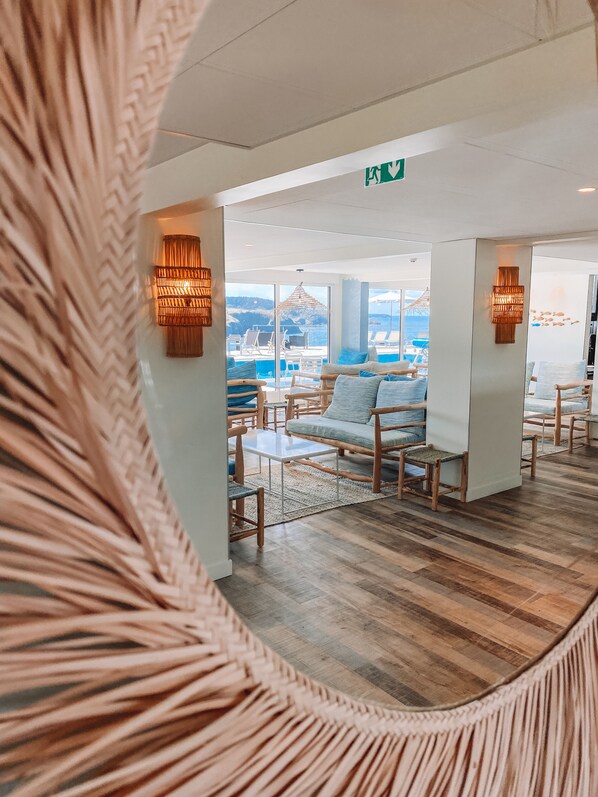 A modern lounge area with a view of the sea, featuring wooden furniture and a glass partition. - Hôtel Le Cardinal (Sauzon)