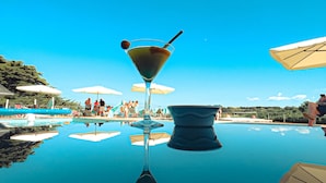 On voit clairement une piscine, avec le reflet d’un verre à martini et d’un parasol.