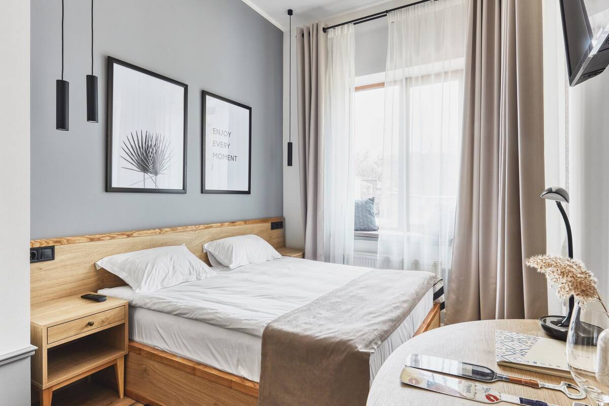Ein modernes Hotelzimmer mit einem Holzbett, einem Nachttisch mit Fernbedienung, einem runden Tisch mit einer Weinflasche, Gläsern und einem Buch.