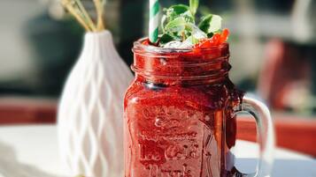 Un bocal en verre avec une paille à rayures vertes et blanches, des feuilles de menthe, des fraises et des myrtilles, le tout posé sur une table blanche.