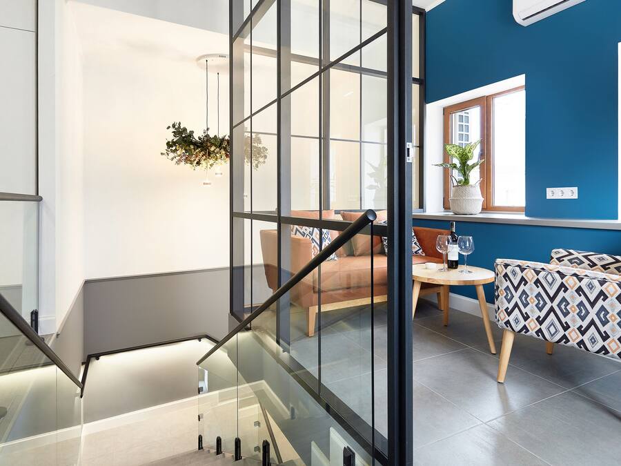 Un interior moderno con una escalera, una zona de estar con una mesa y un ventanal con vistas al exterior.