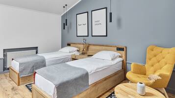 A hotel room with two single beds, a wooden headboard, a yellow armchair, and a small table with a vase.