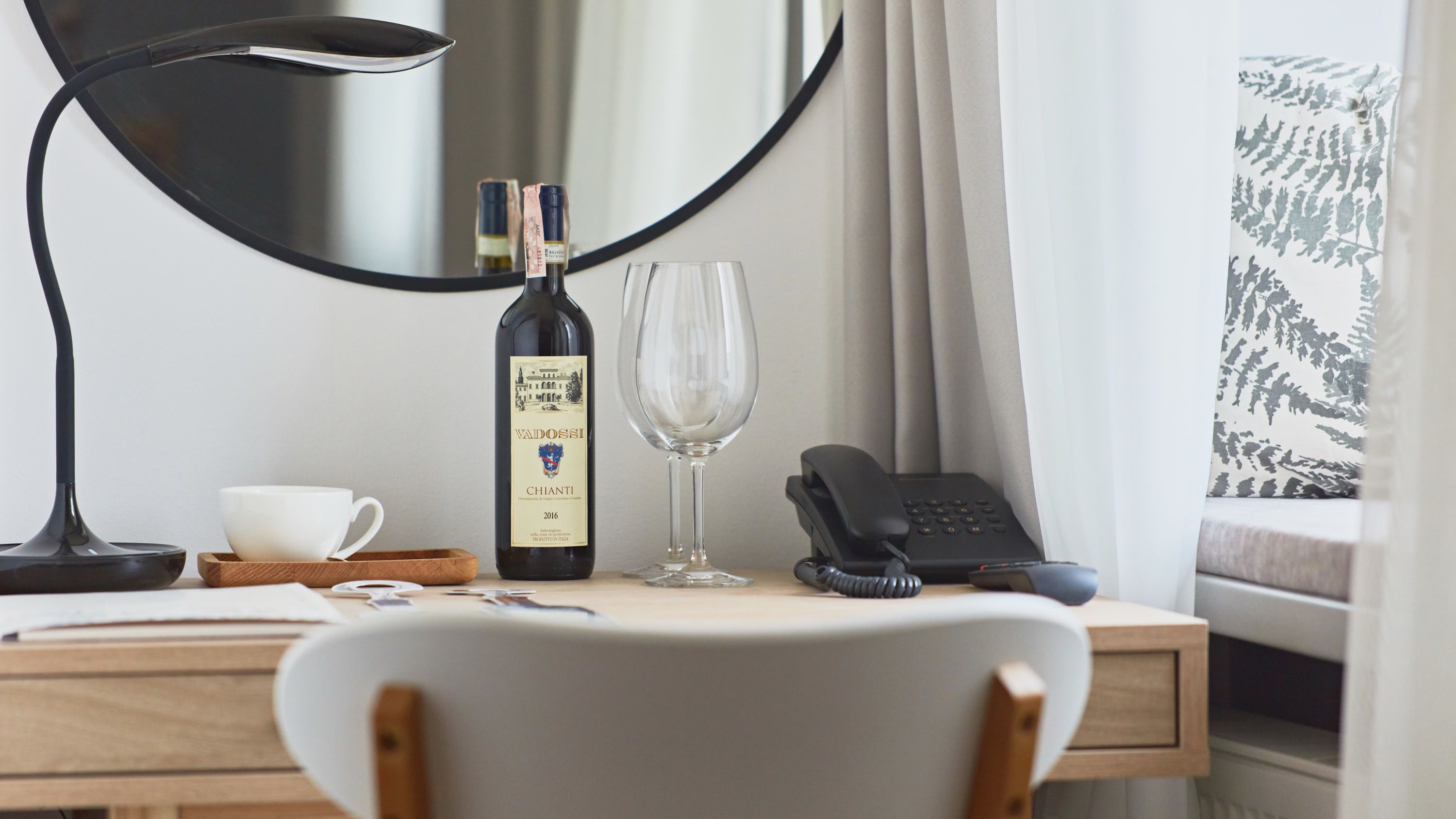 Quarto de hotel com escrivaninha, garrafa de vinho, copo, telefone e cadeira.