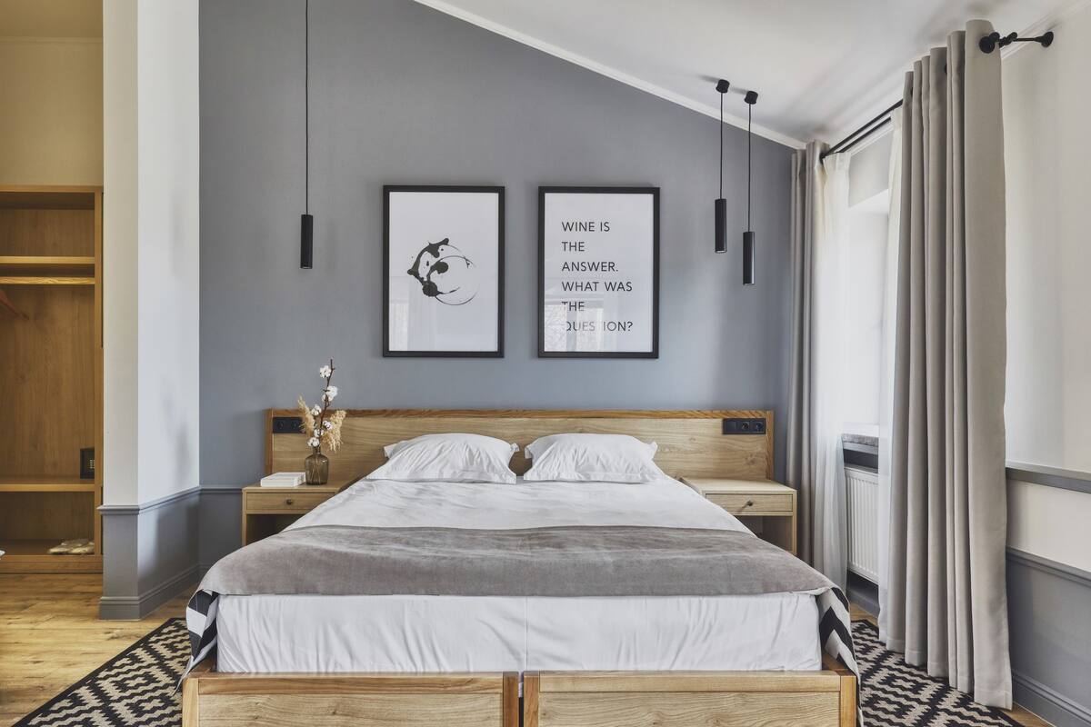 Ein modernes Schlafzimmer mit einem hölzernen Bett, einem Nachttisch, einer Vase mit Blumen und zwei gerahmten Zitaten an der Wand.