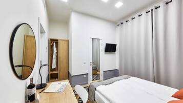 A hotel room with a bed, a desk with a chair, a mirror, a wardrobe, a television, and a curtain.