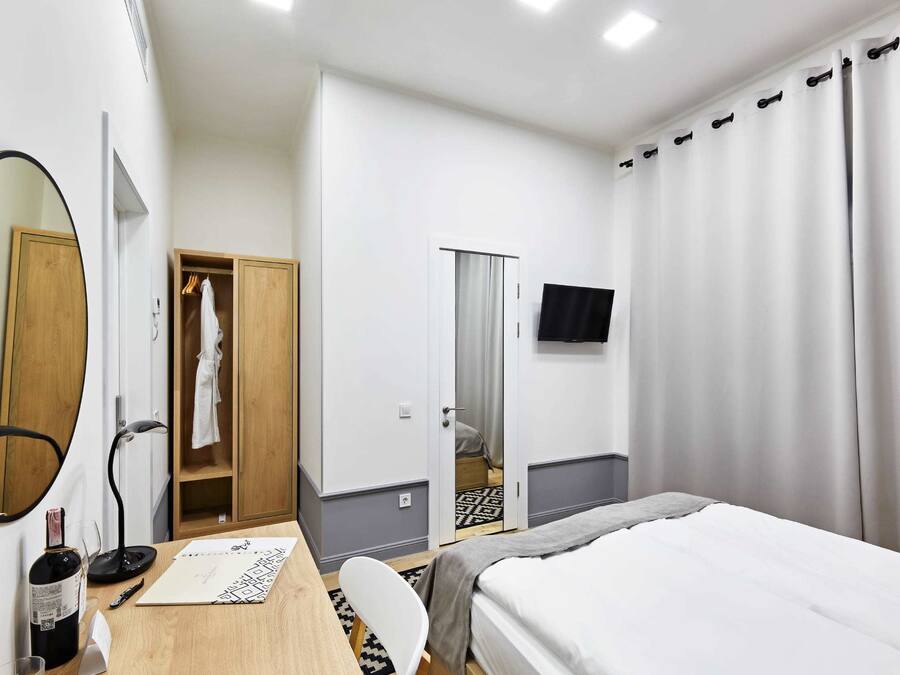 A hotel room with a bed, a desk with a chair, a mirror, a wardrobe, a television, and a curtain.